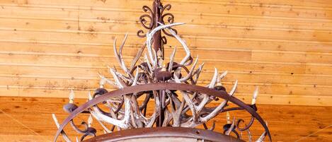 A chandelier with a rustic design, featuring antlers and metalwork, hanging from a wooden ceiling.