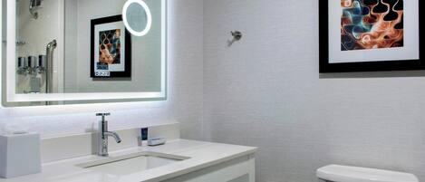 A modern bathroom with a white sink, a large mirror, a framed abstract artwork, and a toilet.