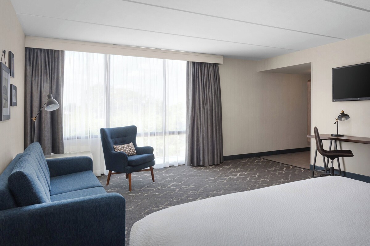 A hotel room with a large bed, a blue sofa, a desk with a chair, and a TV on the wall.
