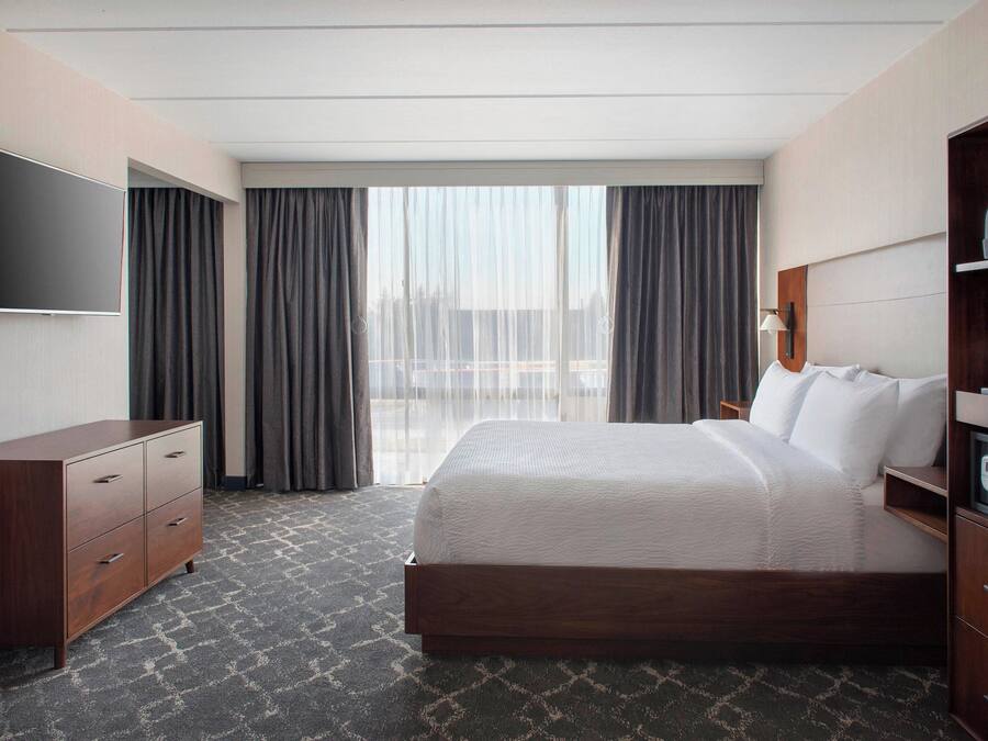 Een hotelkamer met een groot bed, een flatscreen televisie aan de muur, een houten dressoir en een groot raam met gordijnen.