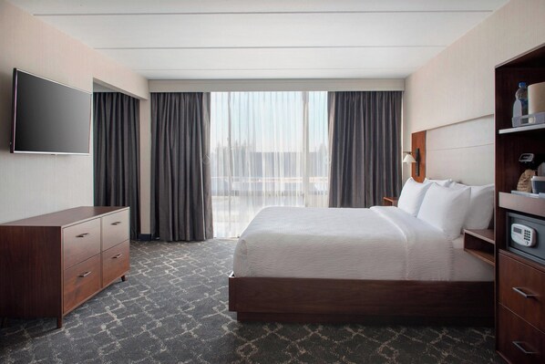 A hotel room with a large bed, a flat-screen TV mounted on the wall, a wooden dresser, and a large window with curtains. - Four Points by Sheraton Philadelphia Northeast (Philadelphia)