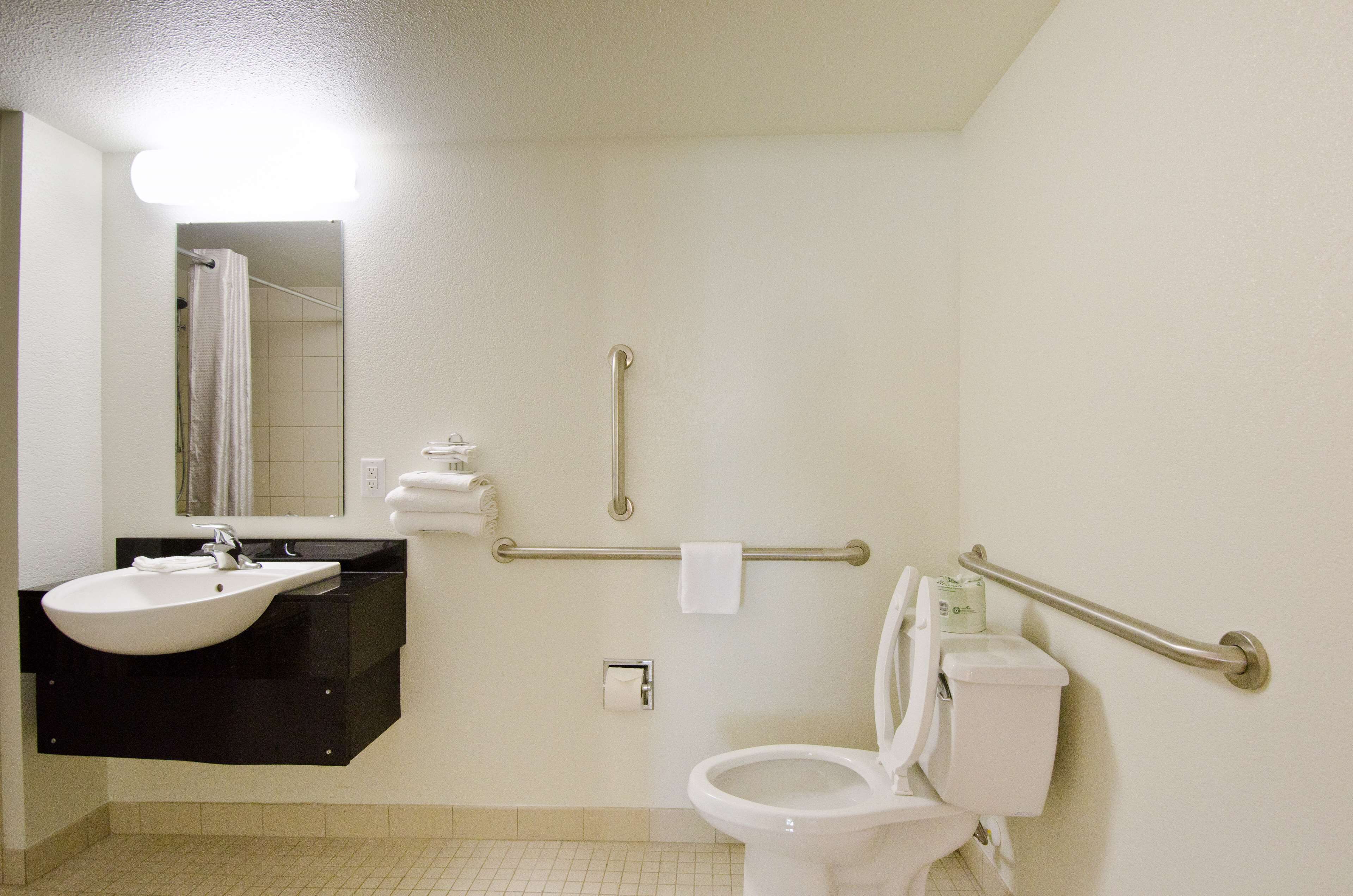 A bathroom with a sink, mirror, toilet, and grab bars.