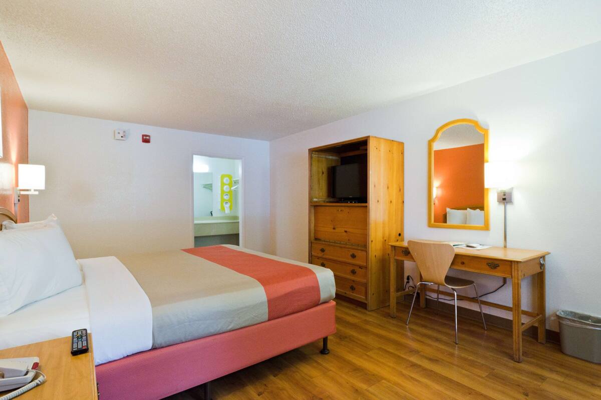 Ein Hotelzimmer mit einem Bett, einem Schreibtisch, einem Sessel, einem Fernseher und einem Spiegel.