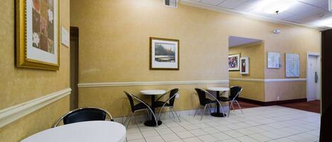 A hallway with a tiled floor, framed pictures on the walls, and tables with chairs.