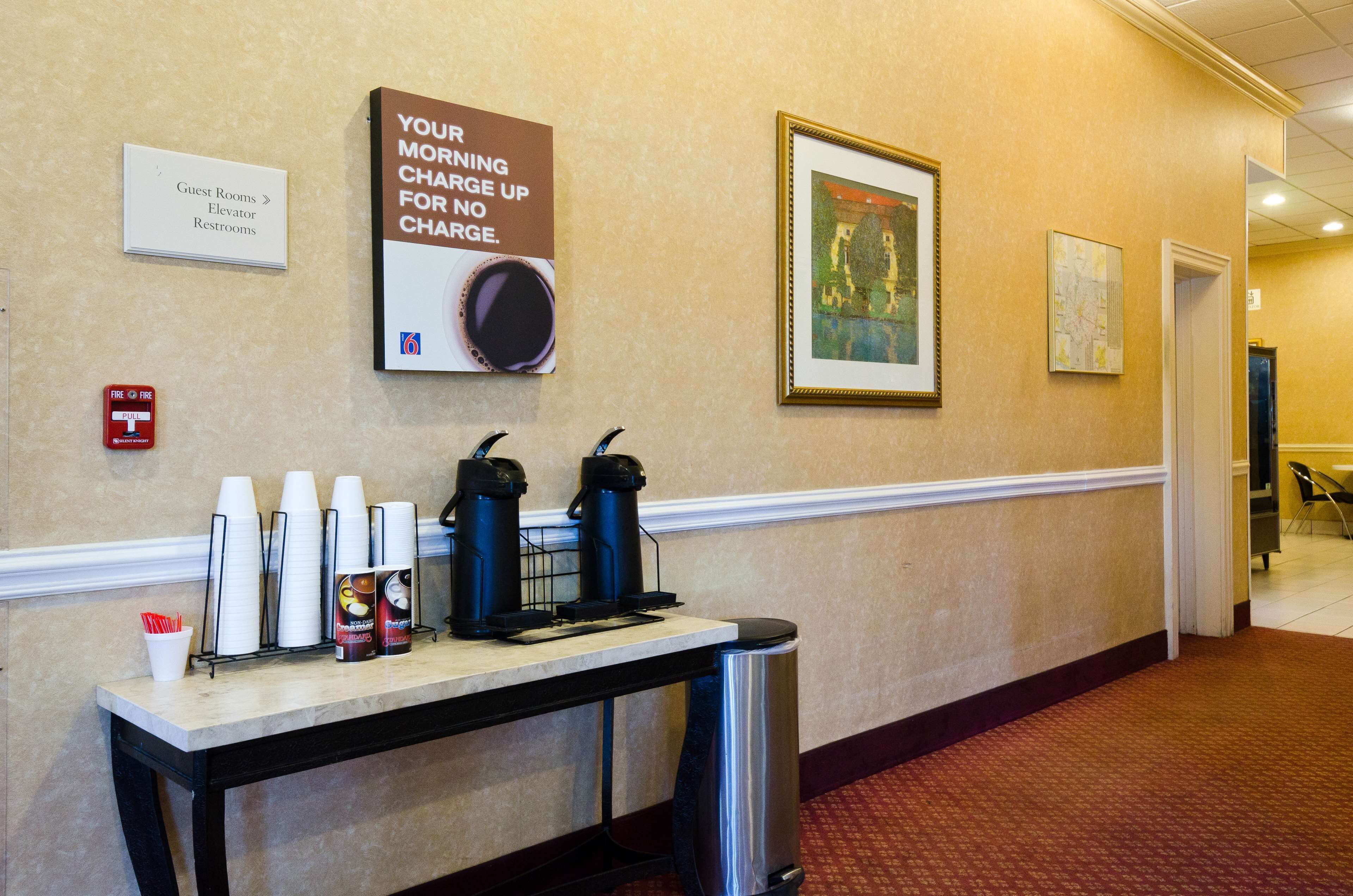 A hotel corridor with a sign indicating guest rooms, an elevator, and restrooms. There are coffee cups and a coffee maker on a table.