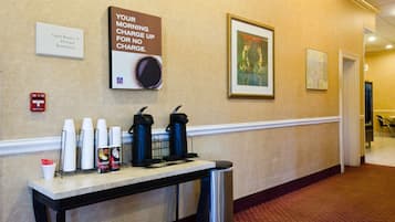 A hotel corridor with a sign indicating guest rooms, an elevator, and restrooms. There are coffee cups and a coffee maker on a table.