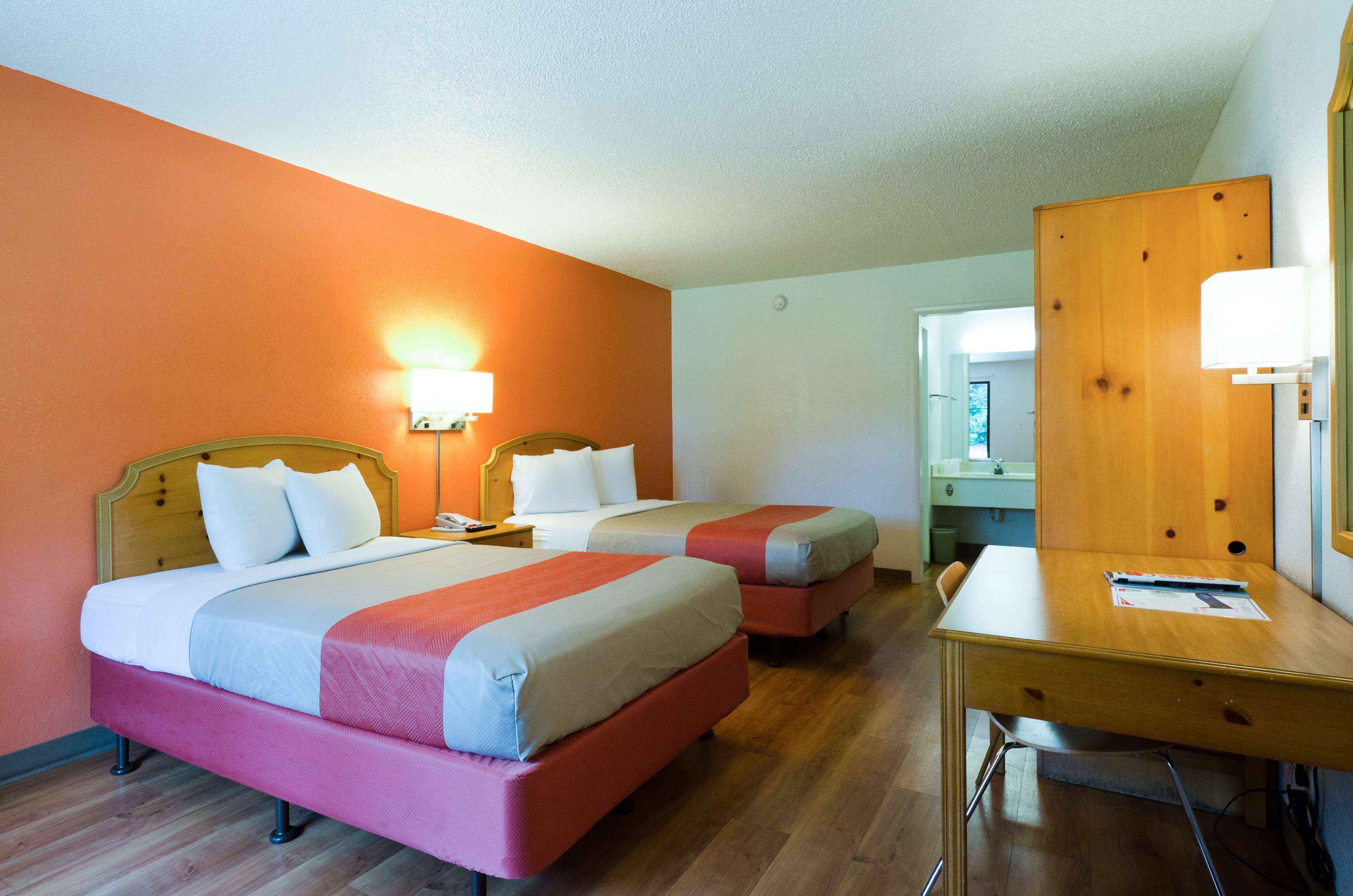 A hotel room with two beds, a desk, and a mirror.