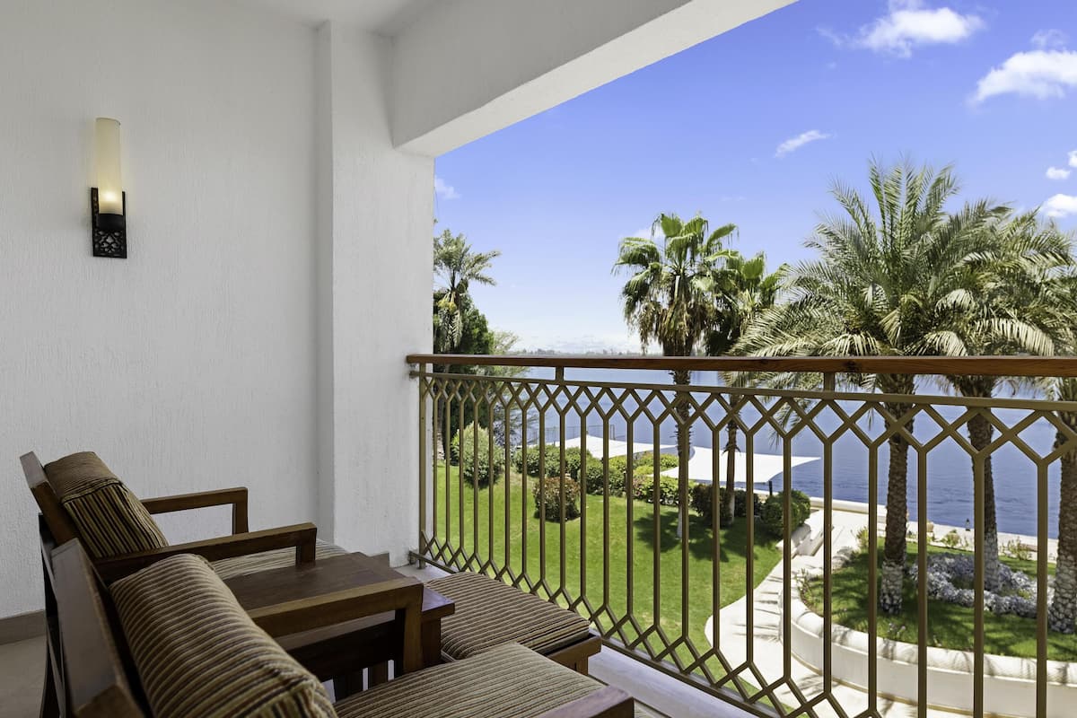 A balcony with a view of the sea, a wooden table, and two cushioned chairs.