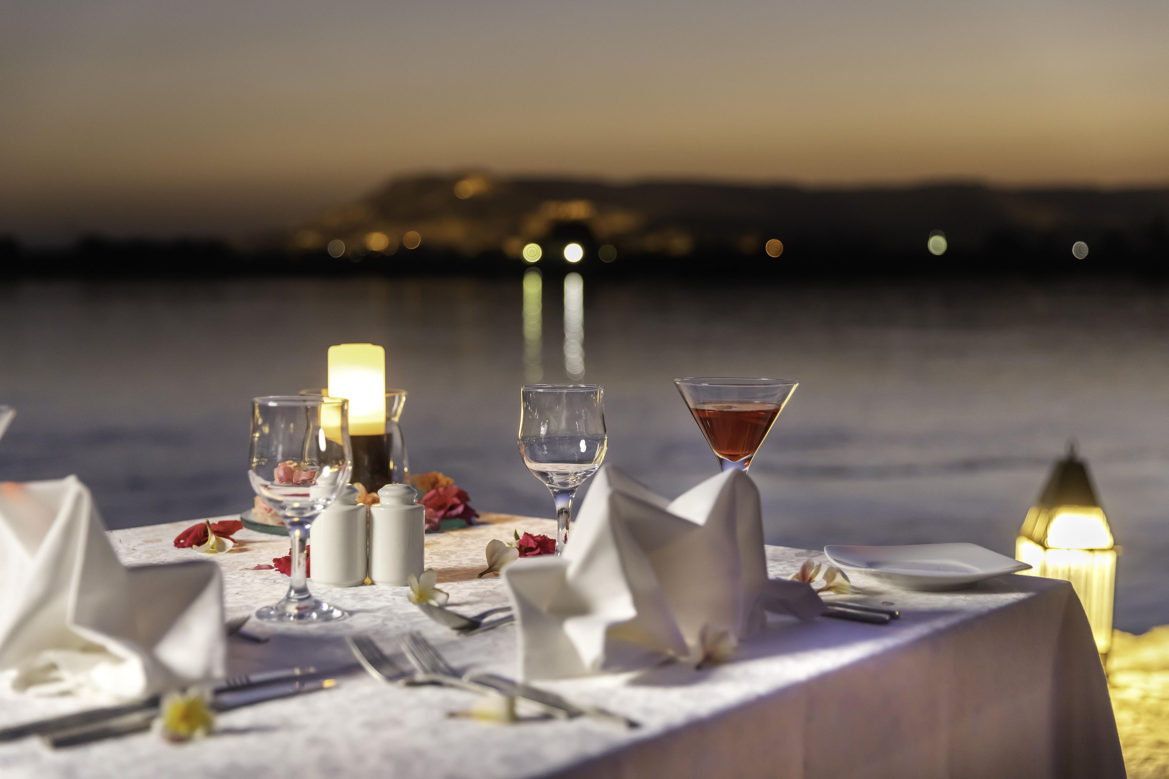 A table set for two with glasses, a candle, and a bottle, overlooking a body of water.