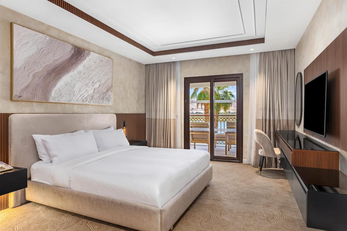 A hotel room with a large bed, a flat-screen TV, a desk, and a view of the outdoors.