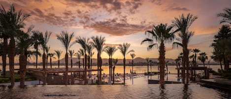 A resort pool area with palm trees and a sunset view.