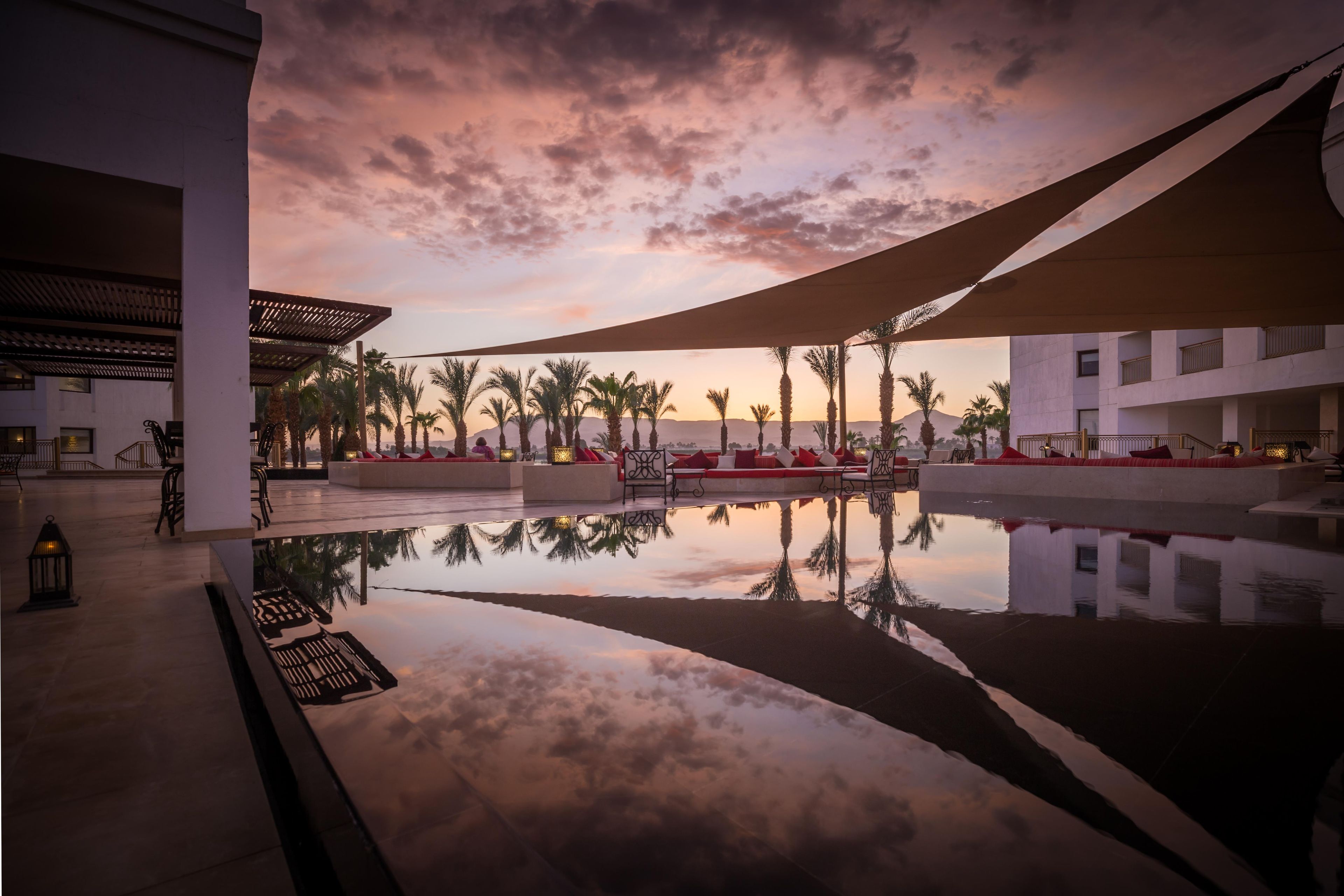 A pool area with a sunset view, palm trees, and modern architecture.