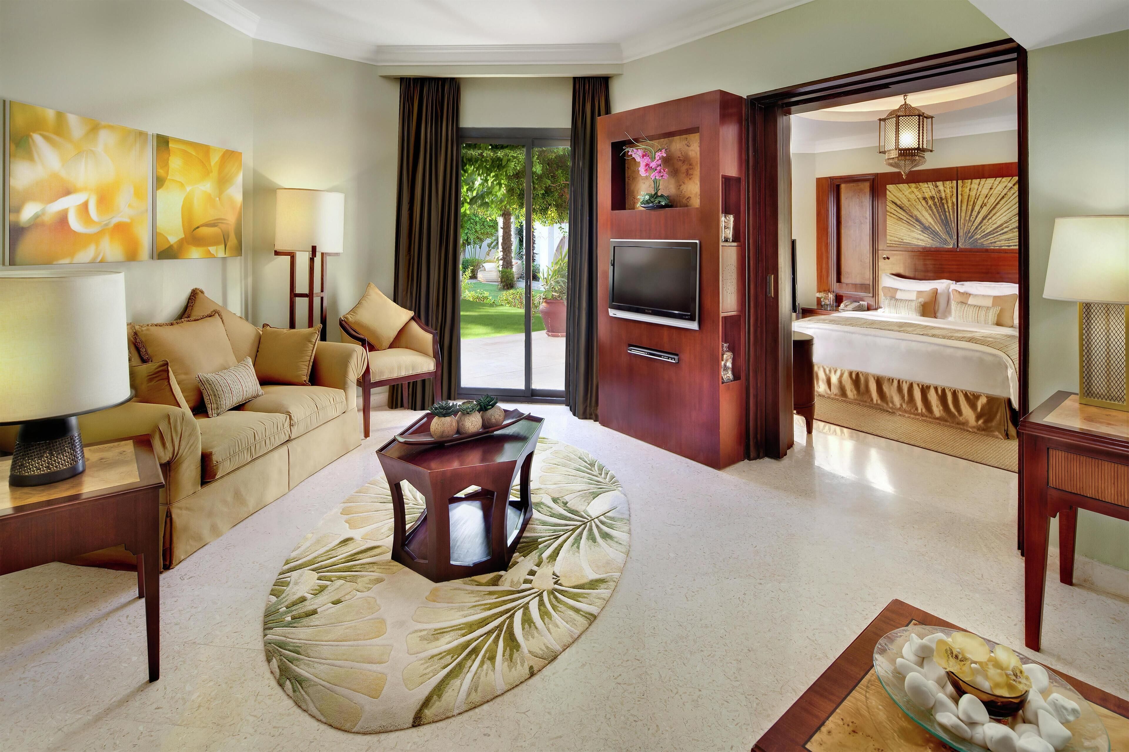 A hotel room with a sofa, a coffee table, a TV, a bed, and a view of the outdoors.