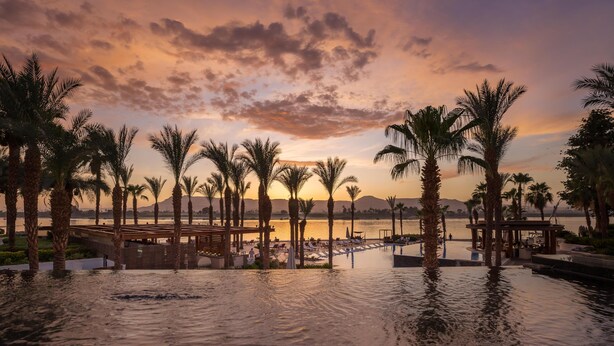 A waterfront resort with palm trees, a pool, and a sunset view. - Hilton Luxor Resort & Spa (Luxor)