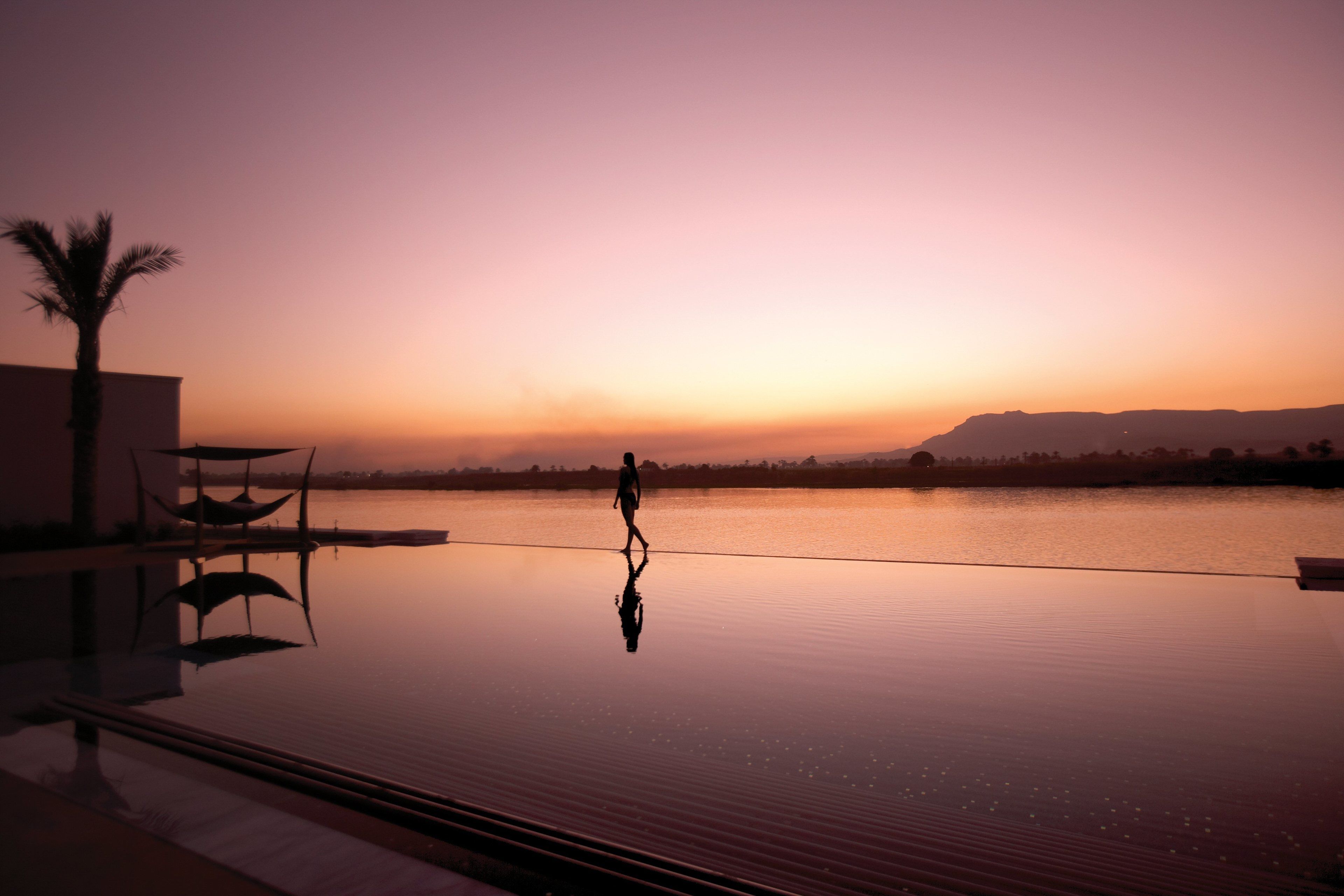 A person walking on a reflective infinity pool at sunset.