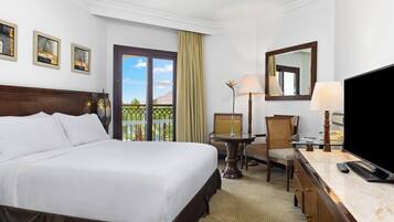 Habitación de hotel con una cama grande, un escritorio con lámpara, una silla, televisión y balcón con vistas.
