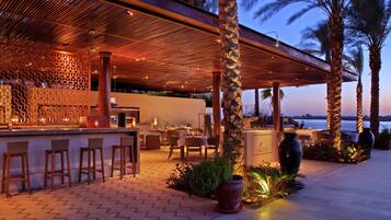 An outdoor bar area with a wooden ceiling, seating, and potted plants.
