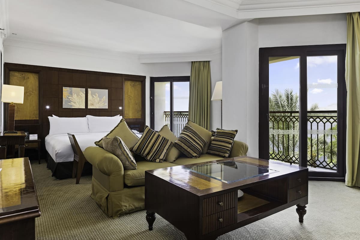 A hotel room with a bed, a sofa, a coffee table, a desk, and a balcony with a view.