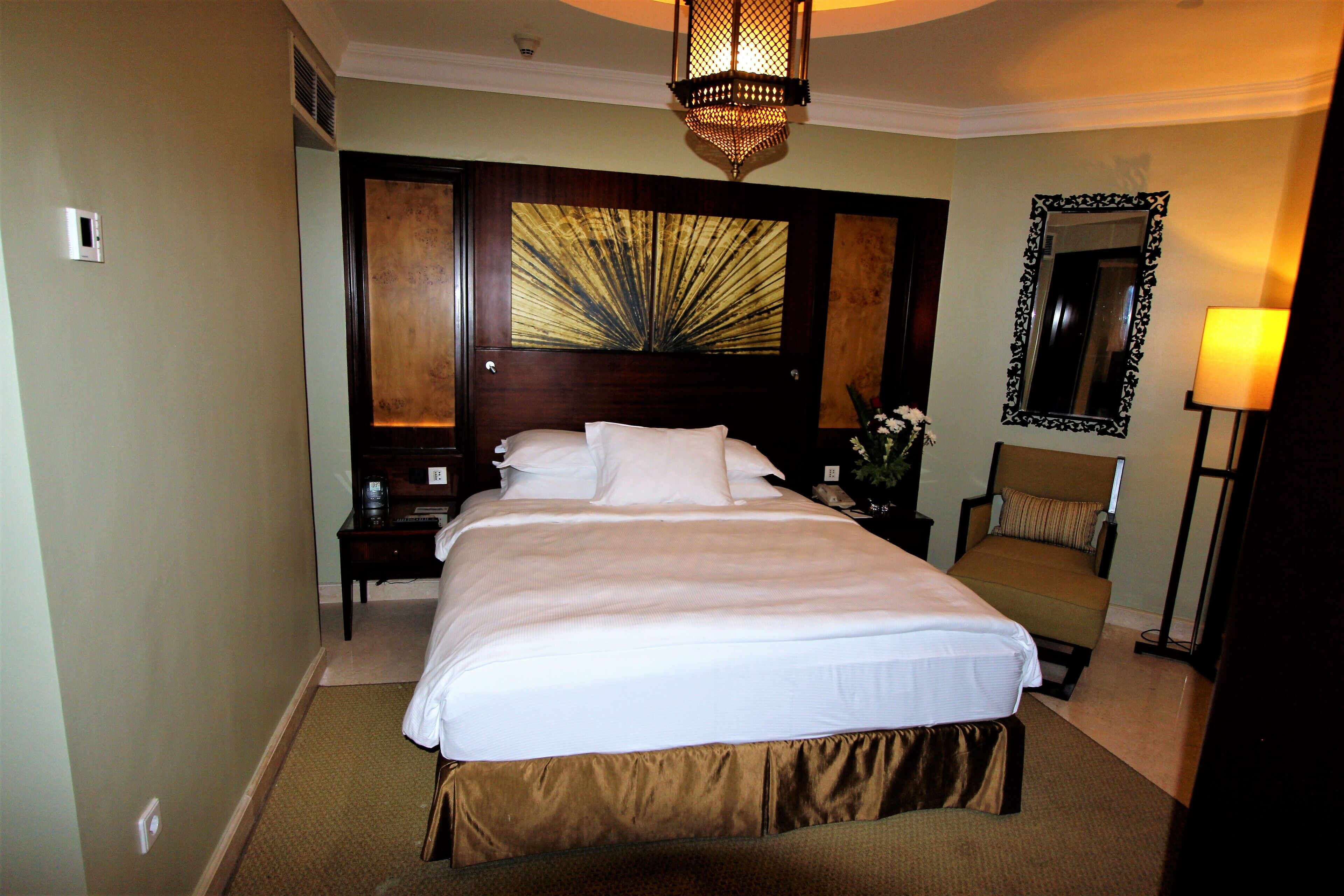 A hotel room with a large bed, a nightstand, a chair, a mirror, and a decorative wall piece.