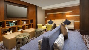 A modern living room with a large flat-screen TV, a sofa with patterned cushions, a coffee table, and a side table. - Skybridge Seattle Airport Hotel (SeaTac)