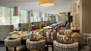 A modern dining area with high tables, upholstered chairs, and pendant lighting. - Skybridge Seattle Airport Hotel (SeaTac)