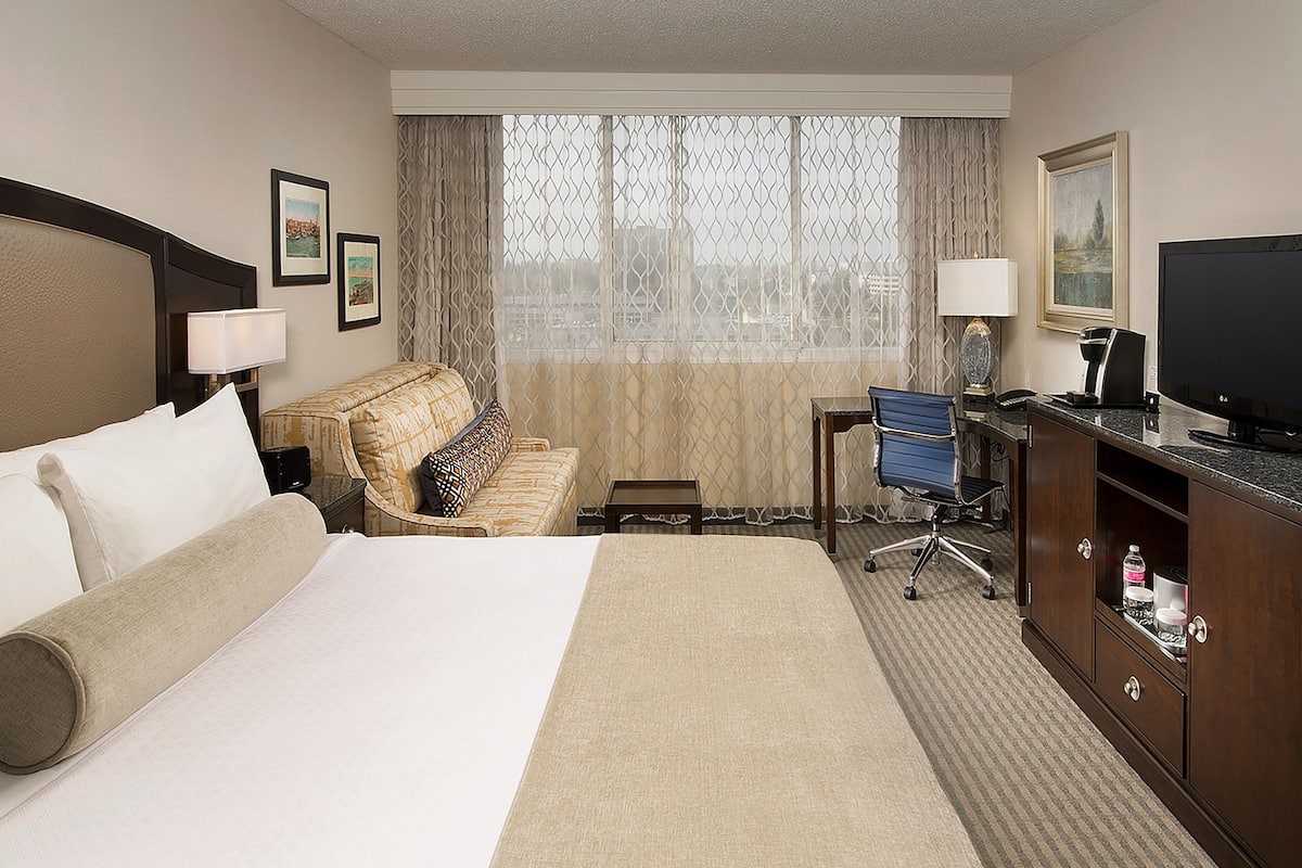 A hotel room with a large bed, a desk with a chair, a television, and a minibar.
