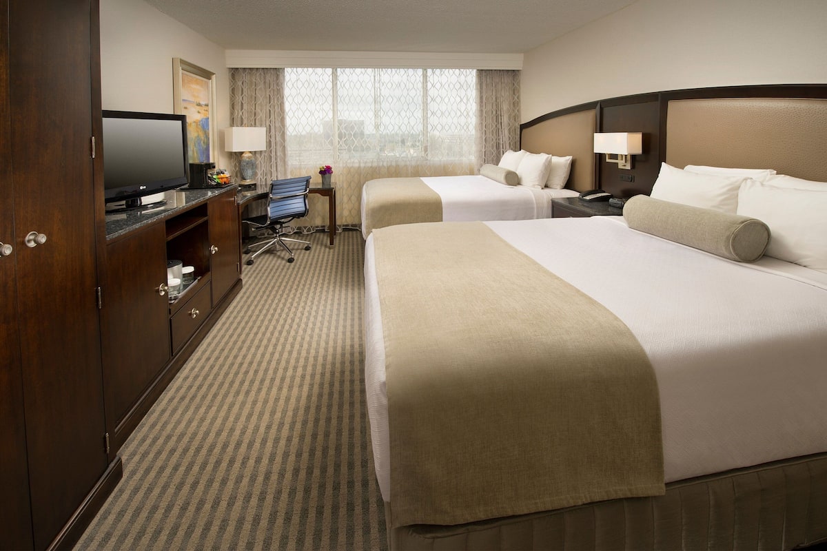 A hotel room with two beds, a desk with a computer, a television, and a window with curtains.