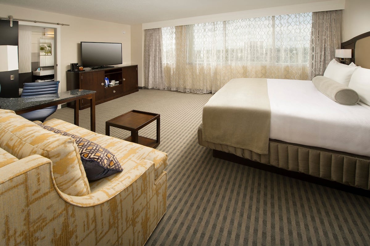 A hotel room with a bed, a sofa, a TV, a desk, and a window with curtains.