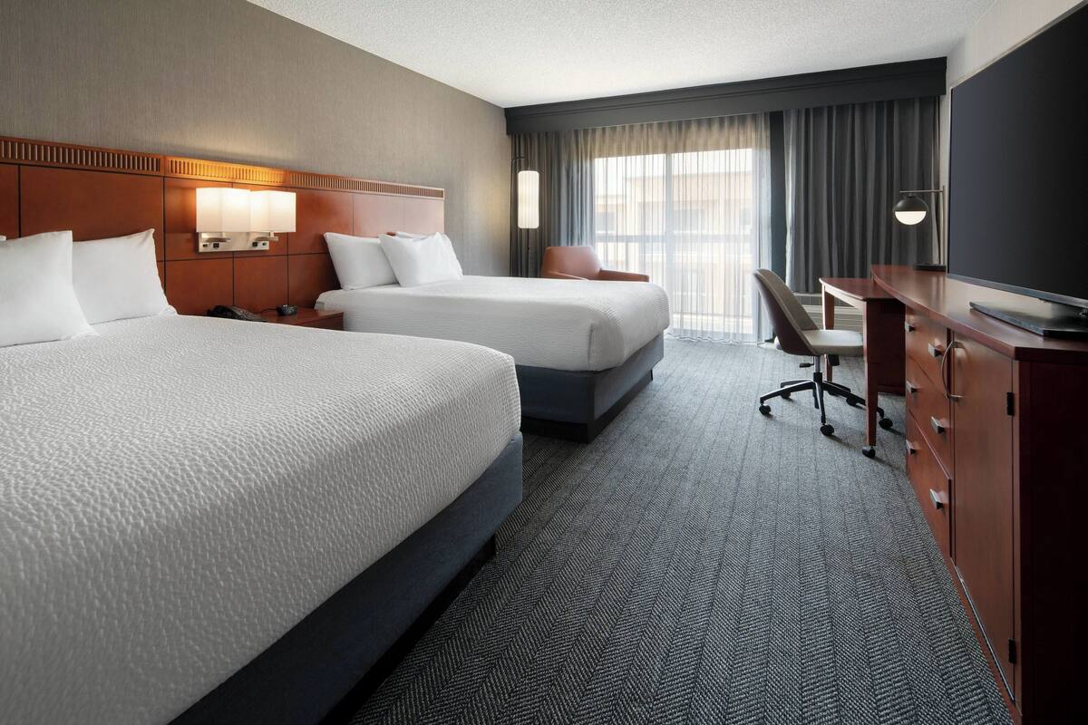 A hotel room with two beds, a desk, a chair, and a television.