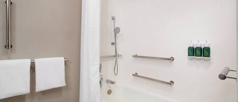 A modern bathroom with a bathtub, shower, and handrails. There are towels hanging on the wall and a shower curtain partially drawn.