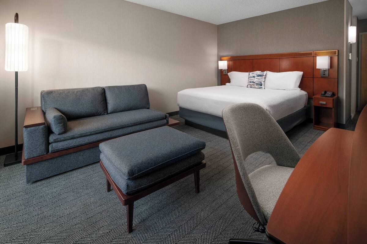 A hotel room with a bed, a sofa, a chair, a desk, and a lamp.