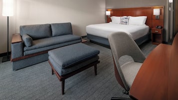 Une chambre d’hôtel avec un lit, un canapé, une chaise, un bureau et une lampe.