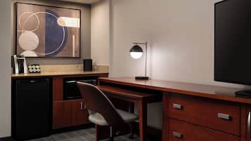 Een hotelkamer met een houten bureau, een stoel, een televisie, een koffiezetapparaat en een koffieautomaat.