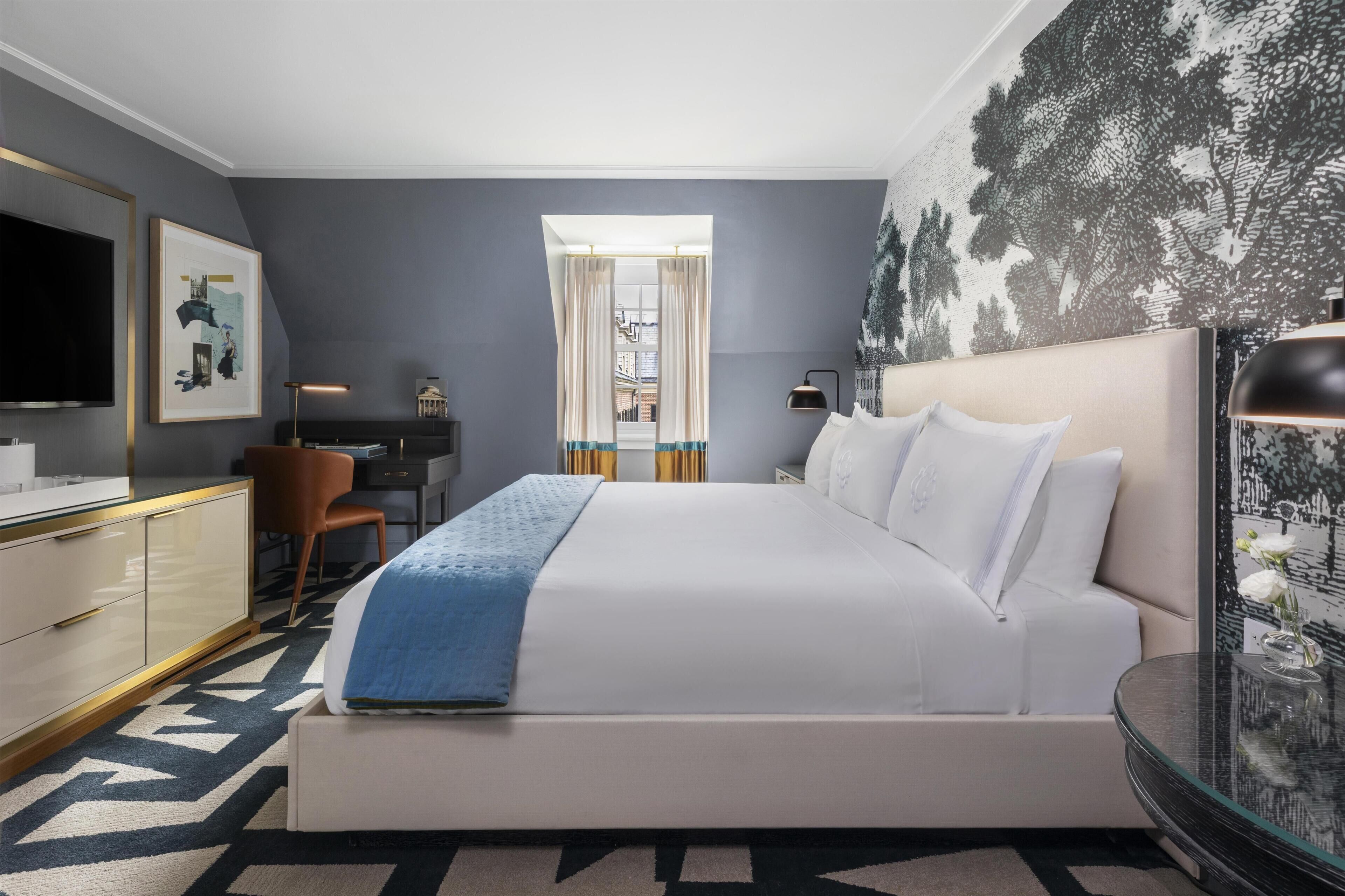 A modern hotel room with a large bed, a desk, a chair, a TV, and a window with curtains.