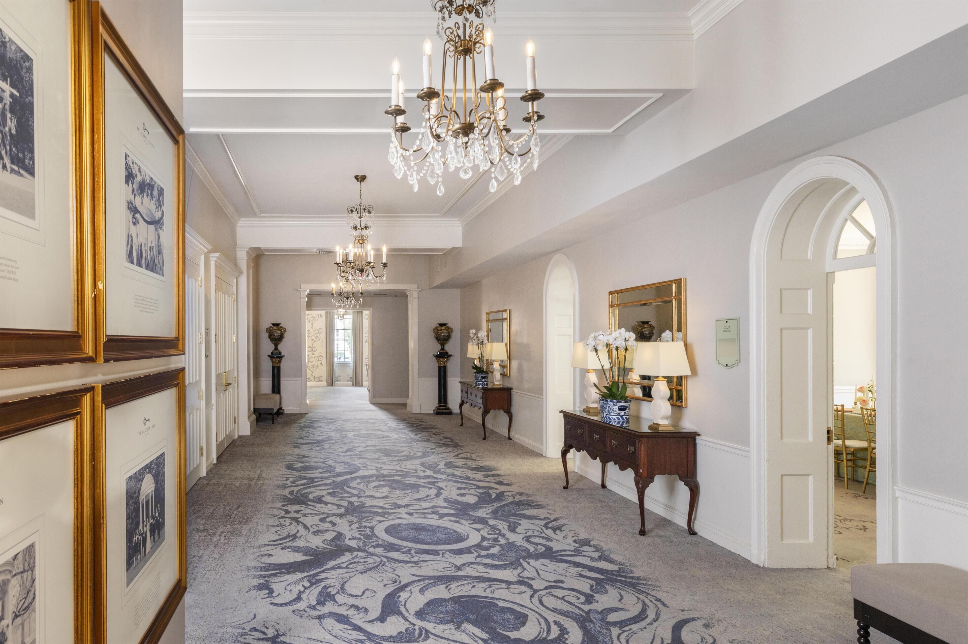 Un vaste hall d’entrée agrémenté d’un tapis à motifs, de lustres, de tableaux encadrés et d’un miroir.