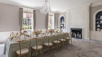 Una sala de dinar formal amb una taula llarga, cadires, un penjallum i una llar de foc.