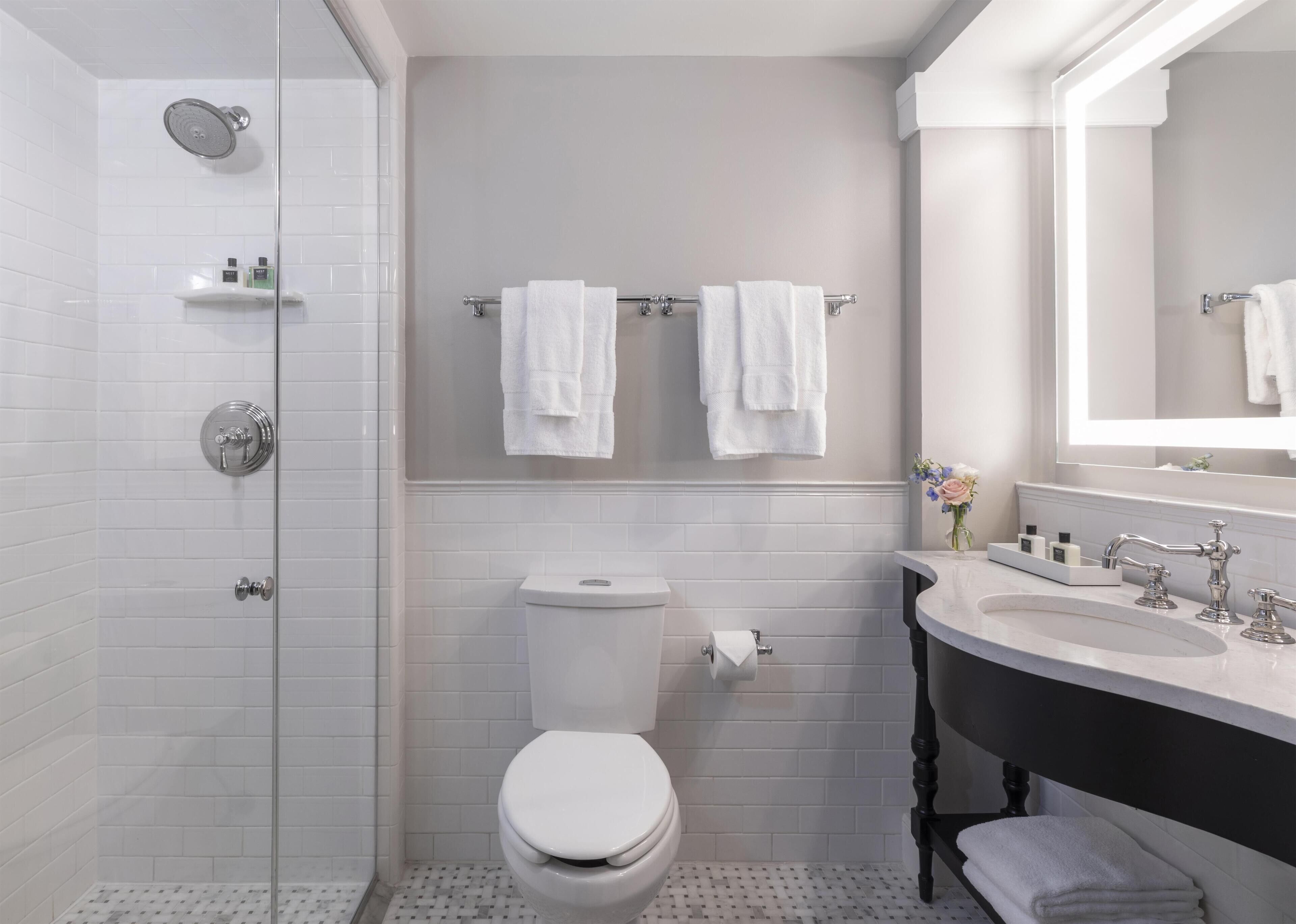Ein Badezimmer mit Duschkabine, Toilette, Waschbecken mit Spiegel und zwei Handtuchhaltern.