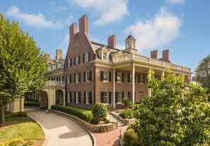 A large brick building with a covered porch, multiple chimneys, and a central tower.