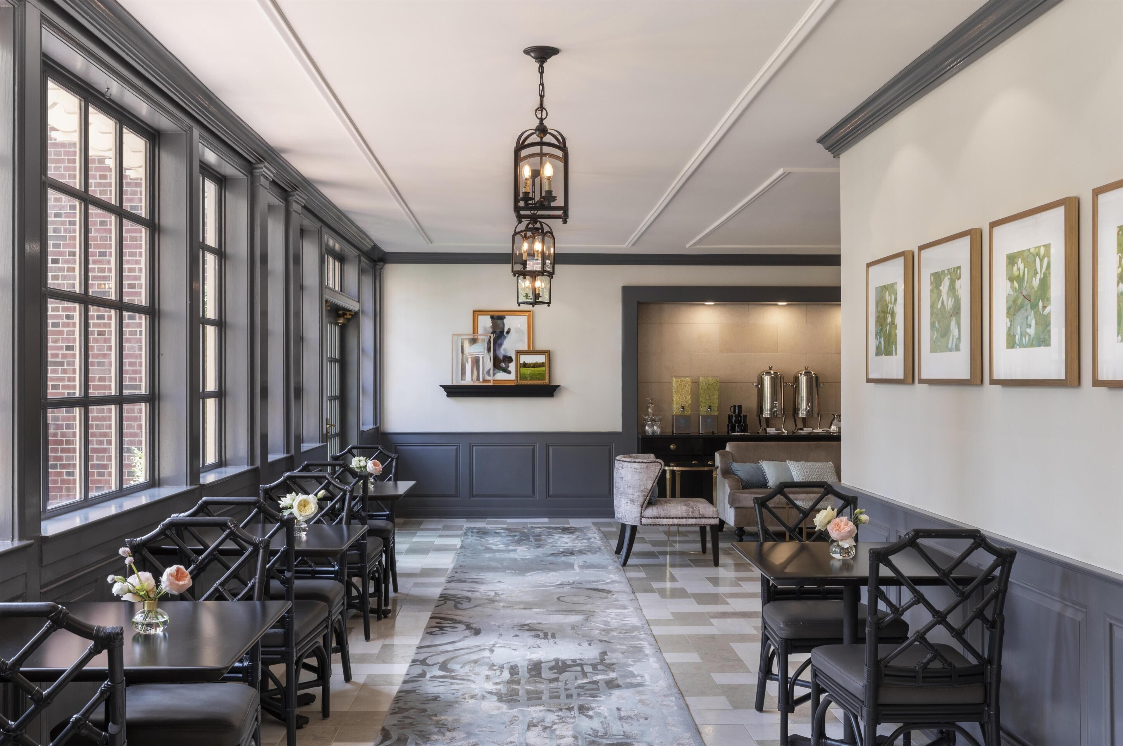 A dining area with long tables and chairs, a chandelier, and framed artwork on the walls.