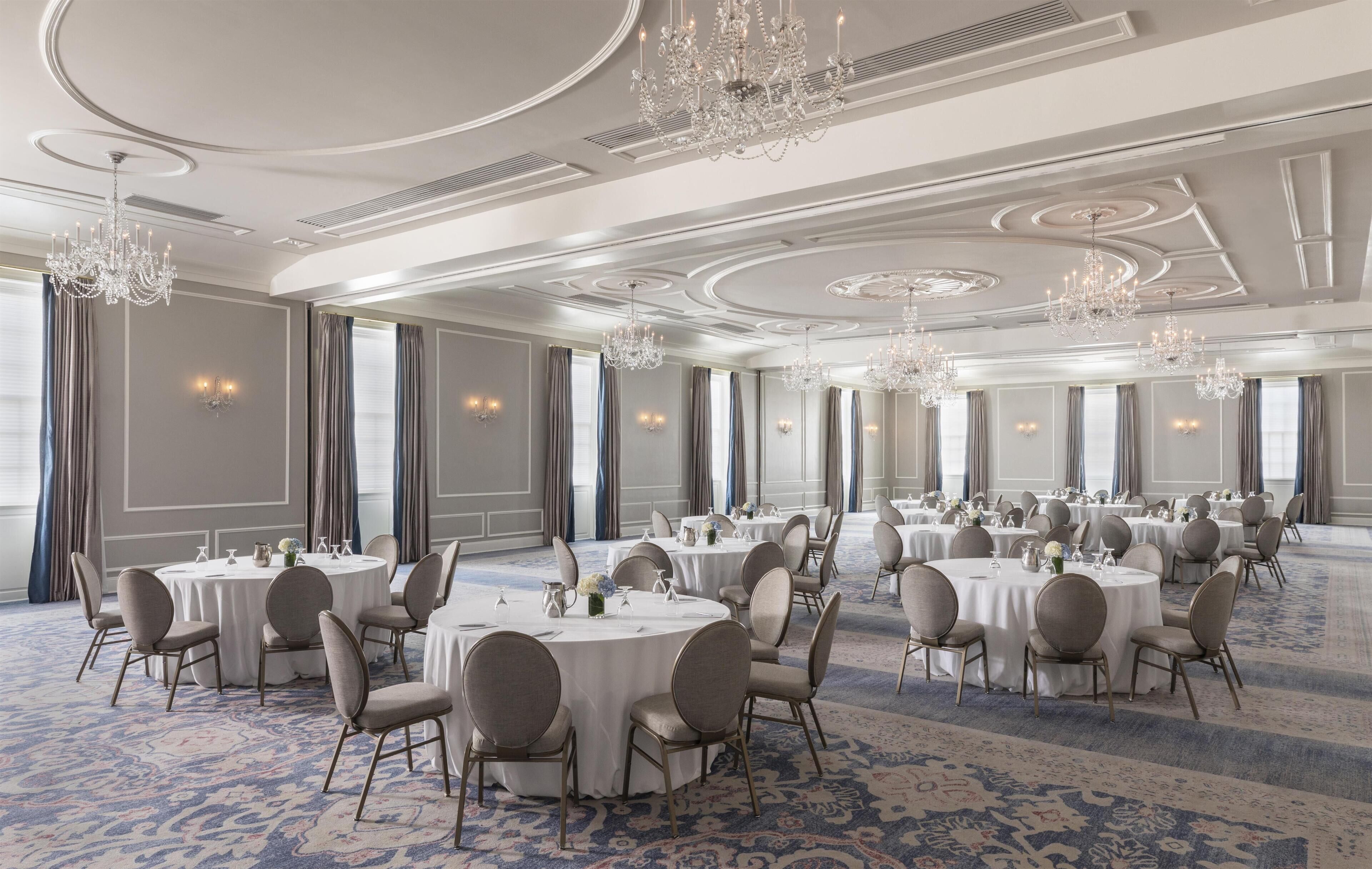 Un amplio salón de banquetes con mesas redondas, sillas, candelabros y una alfombra estampada.