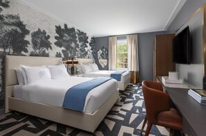 A hotel room with two beds, a desk, a chair, a TV, and a large window with curtains.