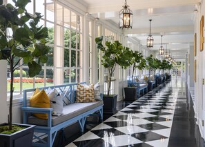 A corridor with a checkered floor, blue benches with cushions, and potted plants. - The Carolina Inn, a Destination by Hyatt Hotel (Chapel Hill)