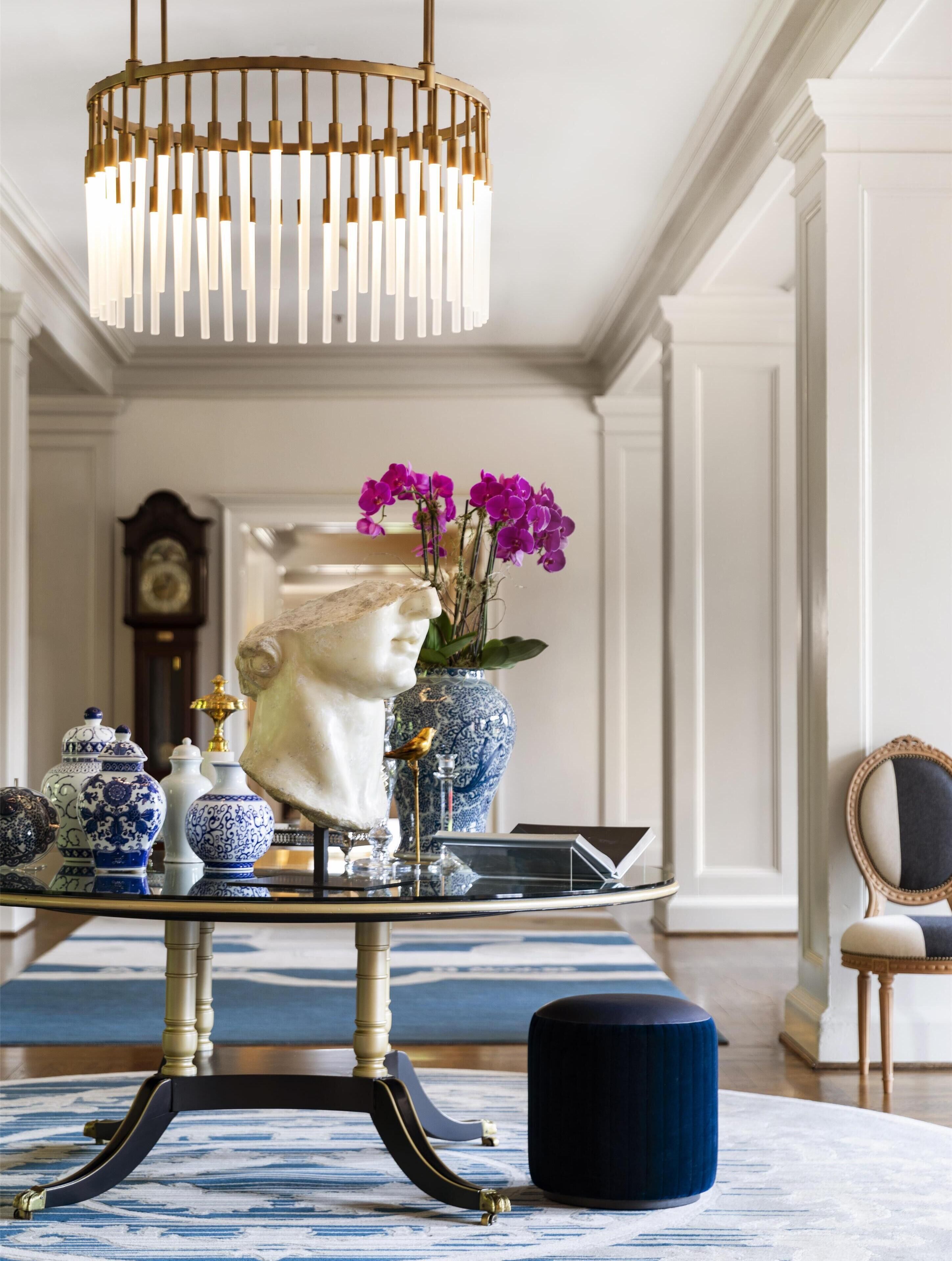 A room with a chandelier, a bust sculpture, and decorative vases on a table.