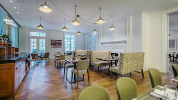A spacious dining area with multiple tables and chairs, a kitchen area with a bar, and a fireplace.