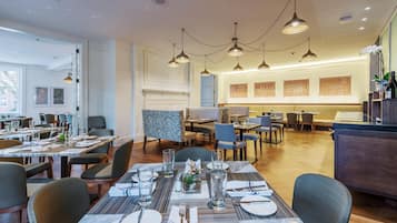Un espace repas moderne, doté de plusieurs tables et chaises, d’un éclairage suspendu et offrant une vue sur la pièce adjacente.