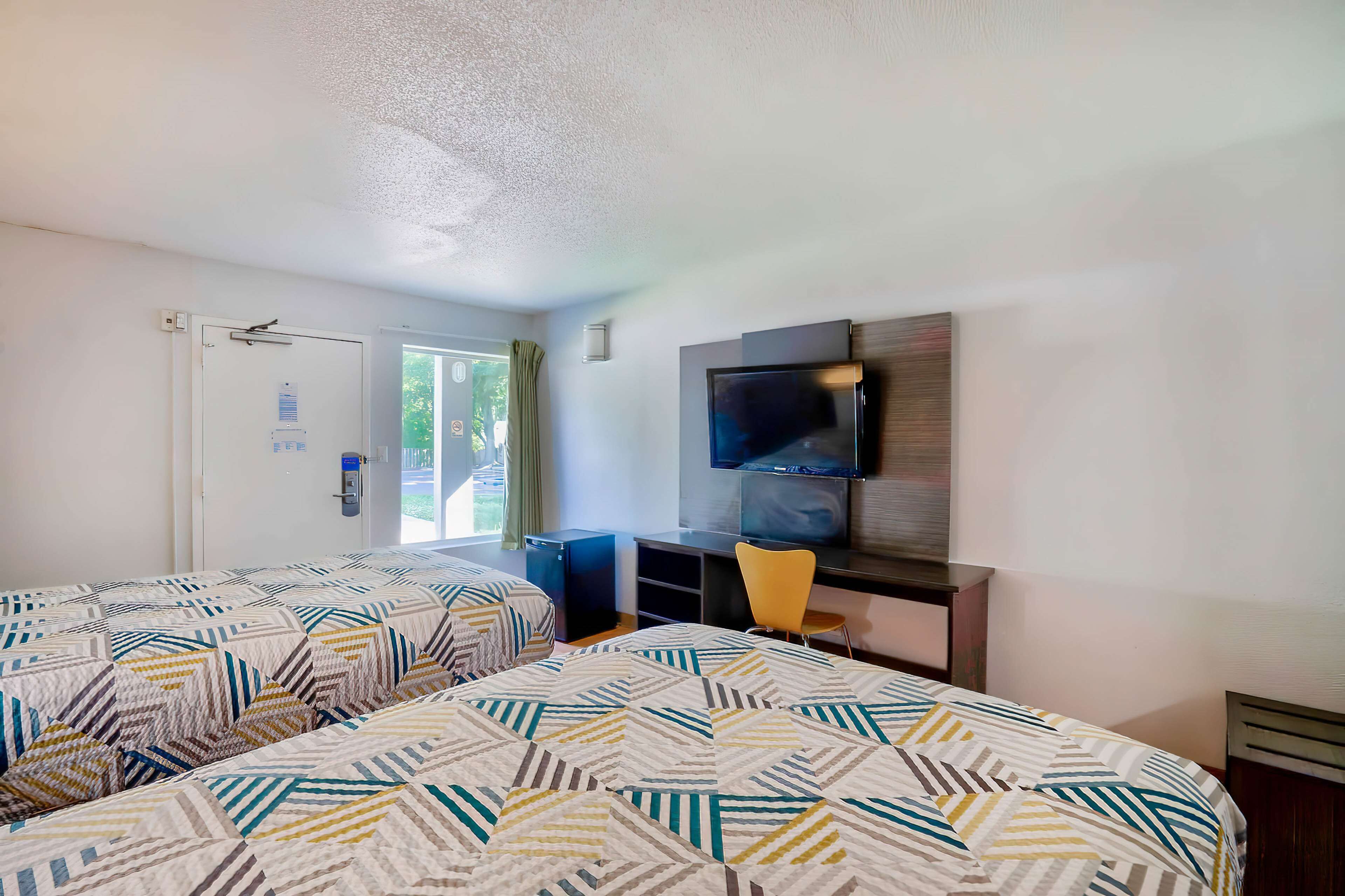 A hotel room with two beds, a TV, a desk, and a chair.