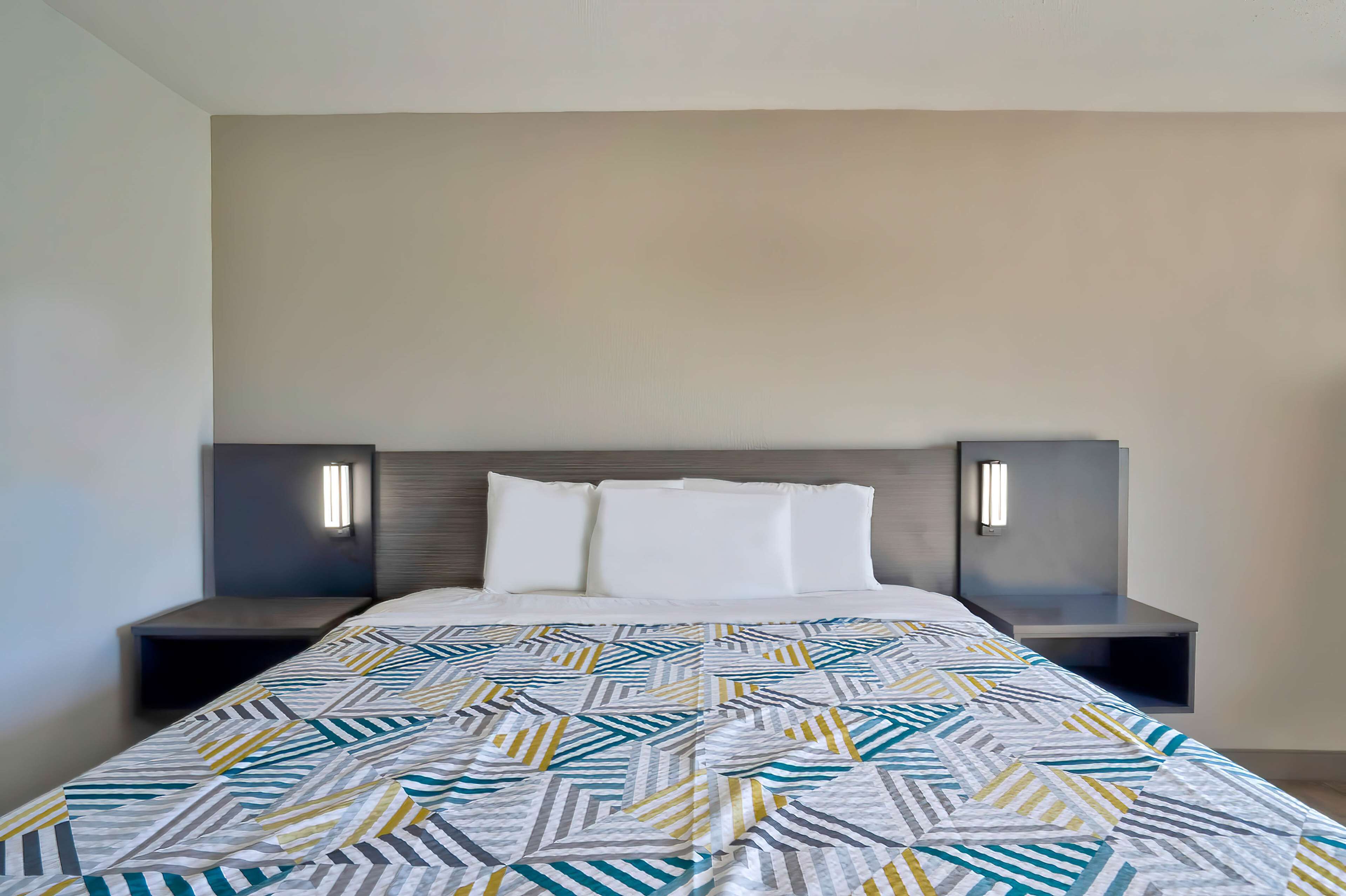 A modern hotel room with a large bed, two bedside tables, and wall-mounted lamps.