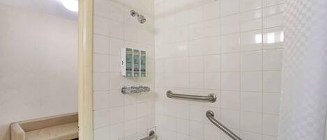 A bathroom with white tiles, a bench, and handrails.