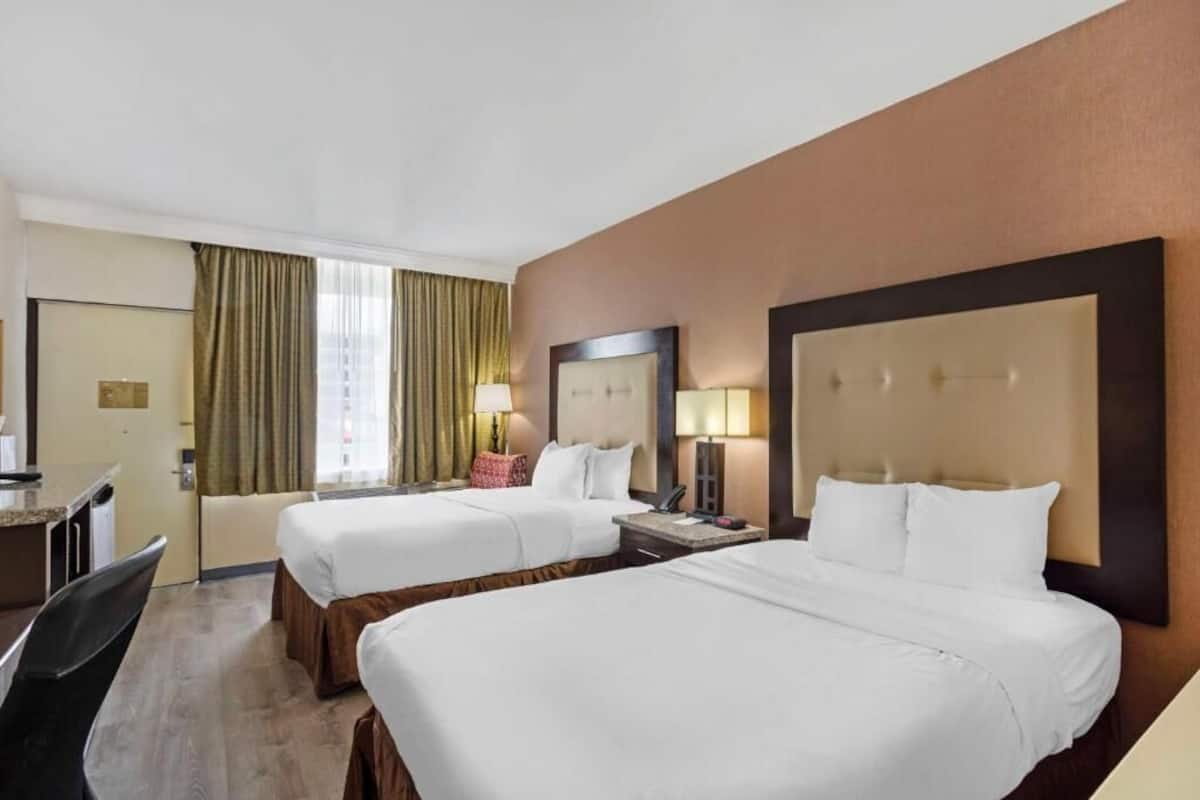 Habitación de hotel con dos camas, un escritorio, una silla, una ventana con cortinas y un espejo.