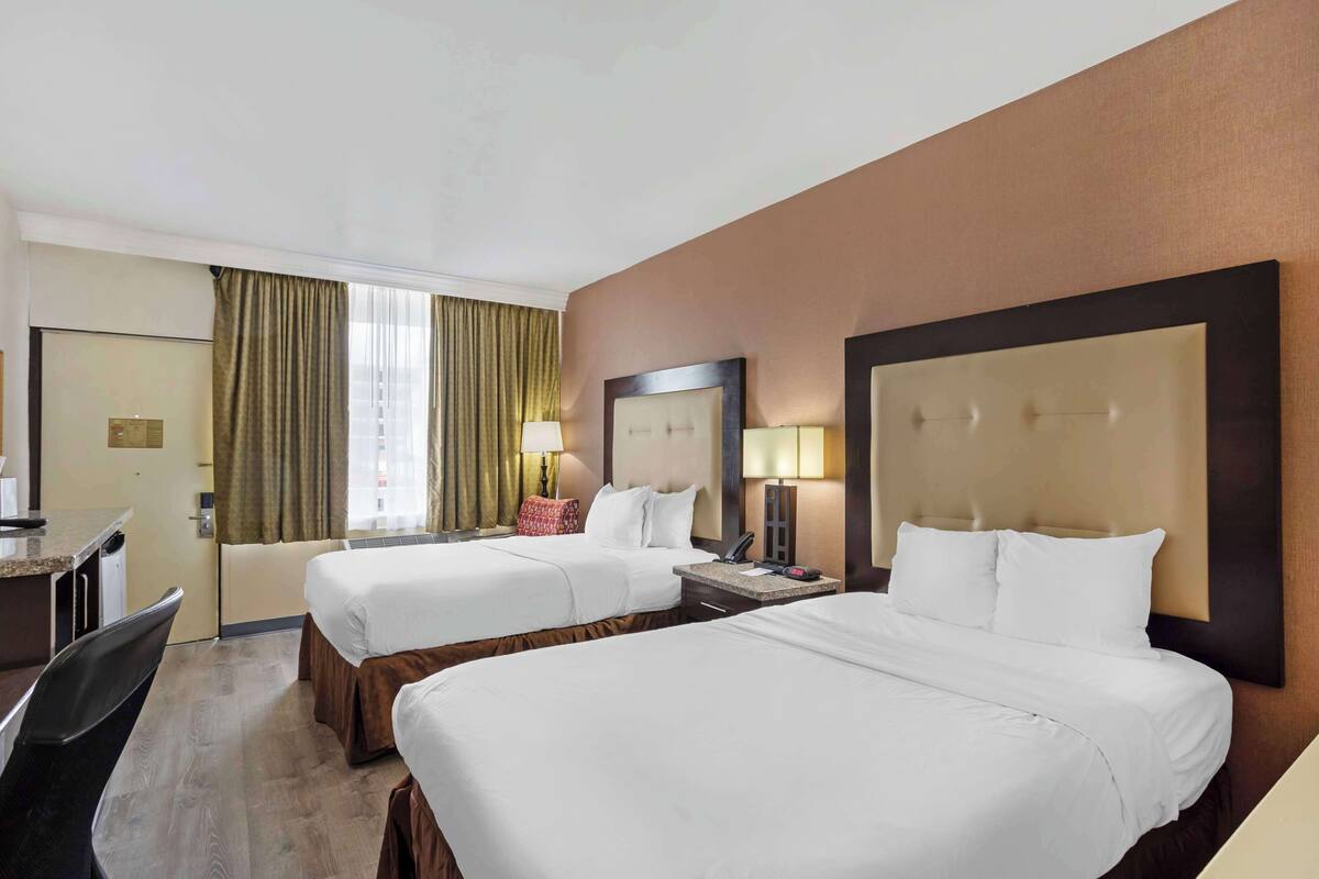 Habitación de hotel con dos camas, un escritorio, una silla, una ventana con cortinas y un espejo.